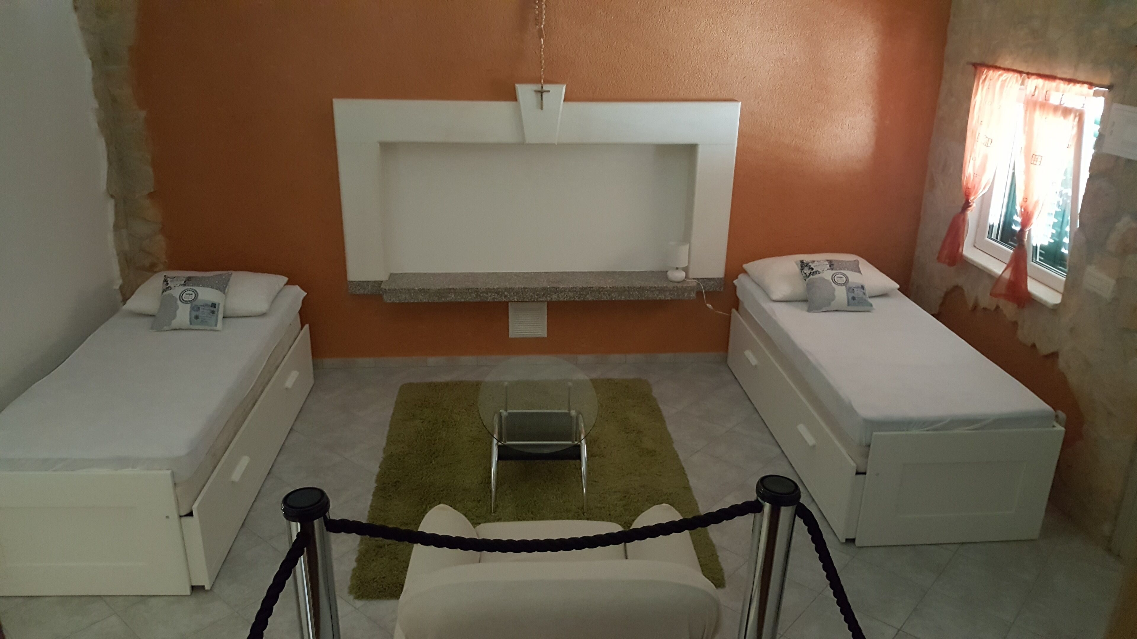 A room with two single beds, a small table, a chair, and a window with curtains.