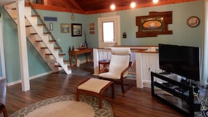 A spacious living room with a wooden staircase, a television, and a sign indicating a boatyard.