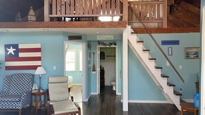 A spacious living area with a high ceiling, a staircase, and a view of the upper floor.