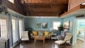 A cozy living room with a wooden ceiling, a sofa with yellow cushions, a coffee table, and a patterned armchair.
