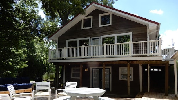 A wooden deck with a picnic table and chairs, a covered seating area, and a balcony with railings.