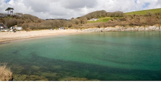 A coastal landscape with clear water, sandy beach, and houses in the background. - Trelawne Garden Annexe (Falmouth)