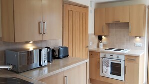 A modern kitchen with wooden cabinets, a built-in oven, a stovetop, a toaster, and a kettle. - Trelawne Garden Annexe (Falmouth)
