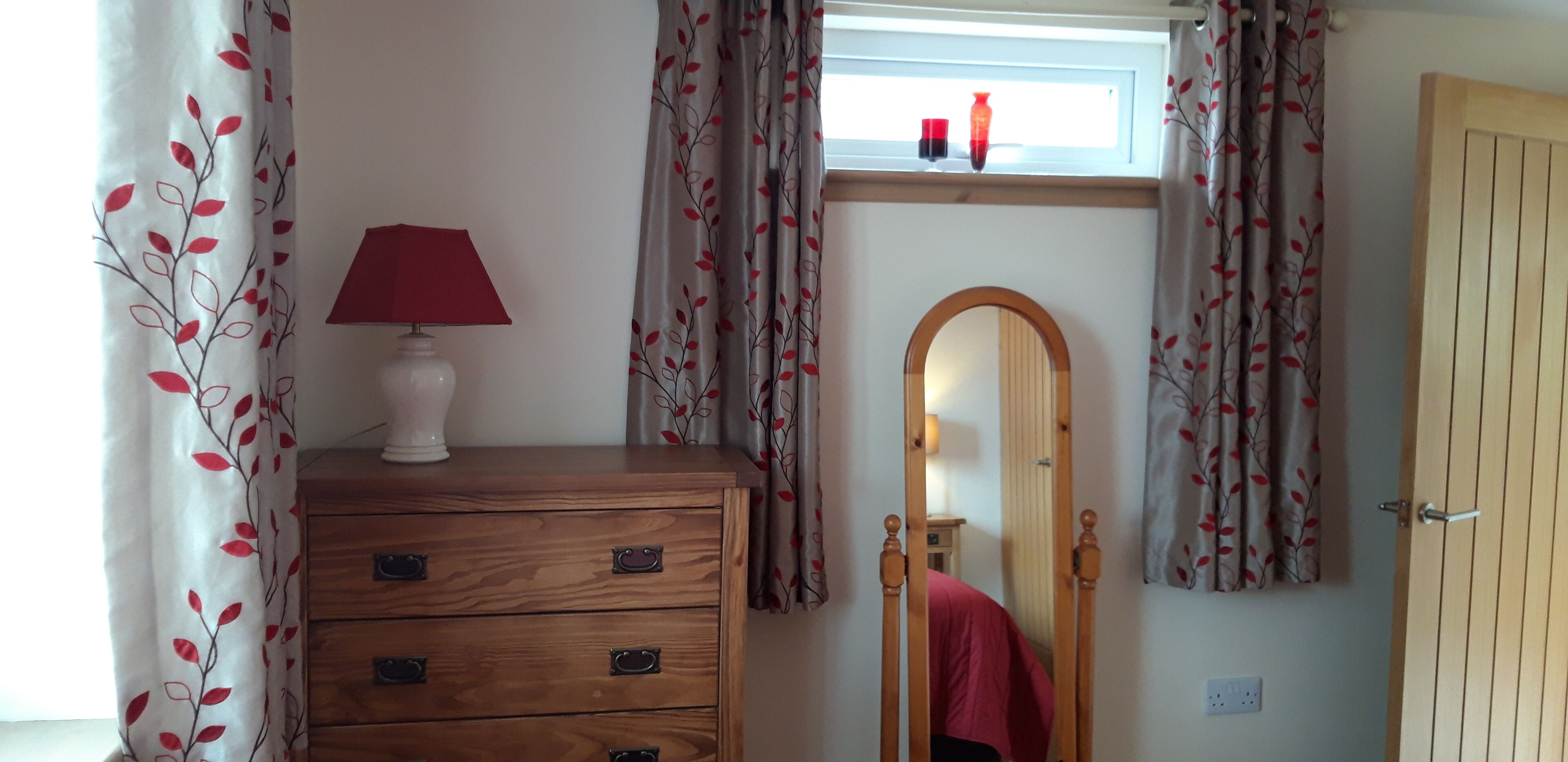 A room with a wooden dresser, a mirror, and a window with curtains.