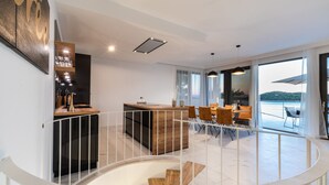 A modern kitchen with a central island, a dining area with a view, and a staircase leading to an upper level. - Villa Desire (Blato)