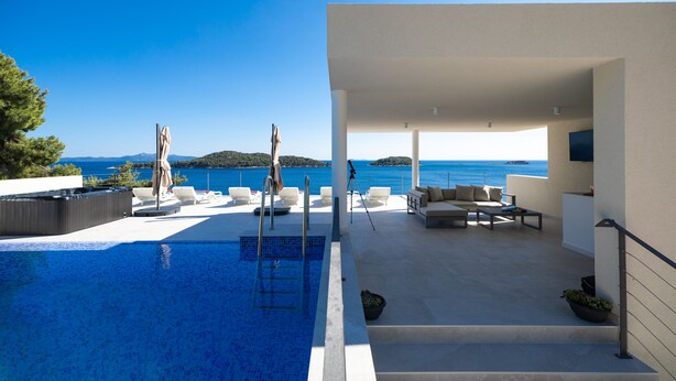 A modern outdoor pool area with lounge chairs and a sofa, overlooking a clear blue sea. - Villa Desire (Blato)
