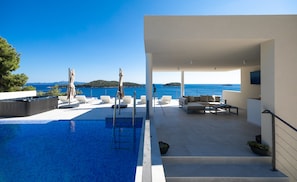 A modern outdoor pool area with lounge chairs and a sofa, overlooking a clear blue sea. - Villa Desire (Blato)
