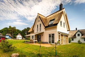 Une maison avec un toit de chaume, de grandes fenêtres et un patio couvert.