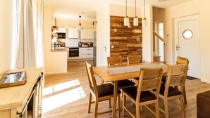 A modern kitchen with wooden cabinets, a dining table with chairs, and a wooden accent wall. - Fuchsbau (Zirchow)