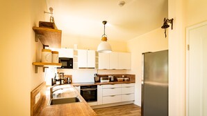 A compact kitchen with white cabinets, a wooden countertop, a stainless steel refrigerator, and a hanging pendant light. - Fuchsbau (Zirchow)