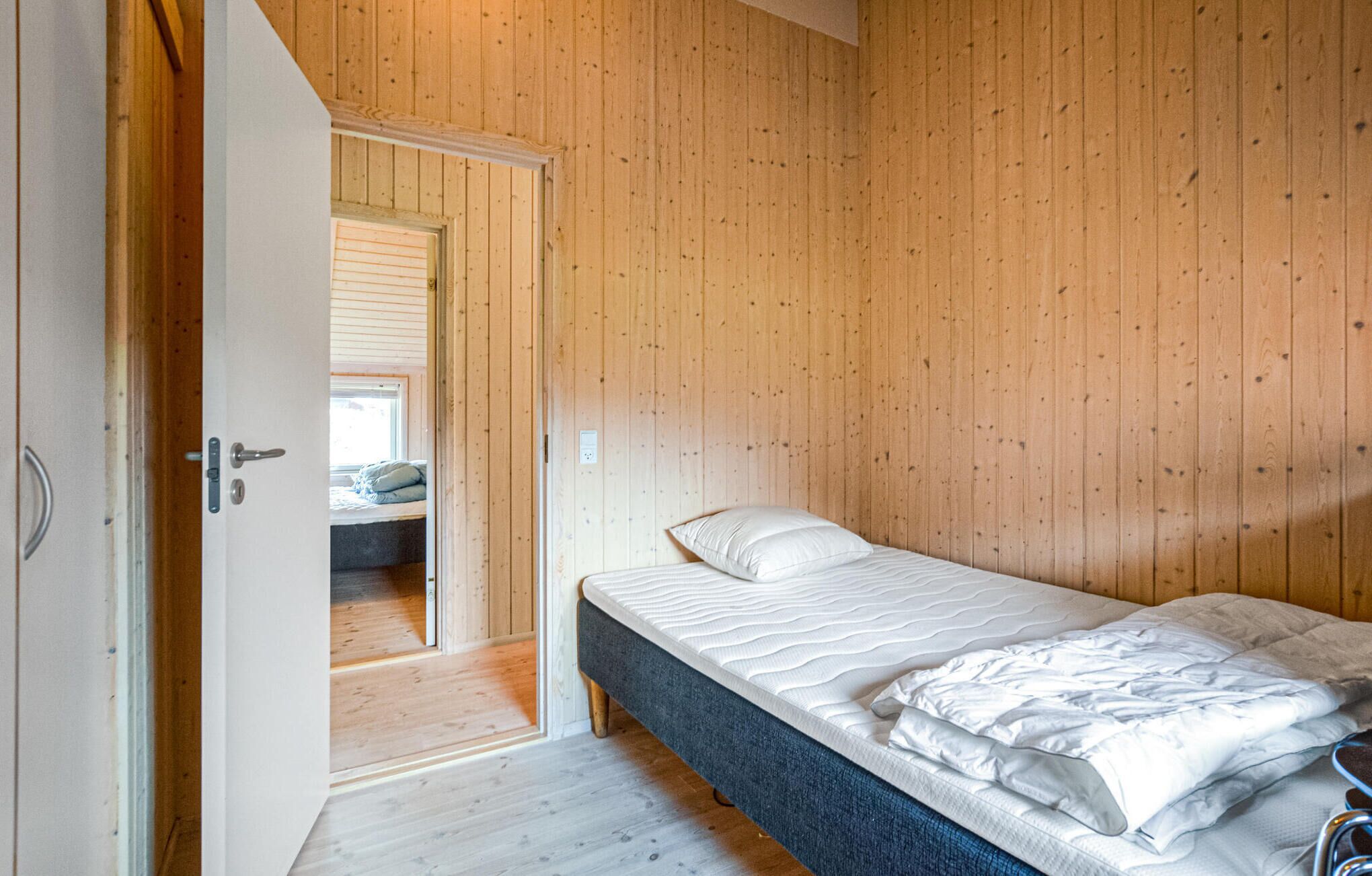 Une chambre avec un mur lambrissé en bois, un lit avec une literie blanche et une porte donnant sur une autre pièce.