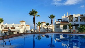 A swimming pool with a clear blue water surface, surrounded by white buildings with red-tiled roofs and palm trees. - Marina Alcaidesa 2305 Luxury Golf House (San Roque)