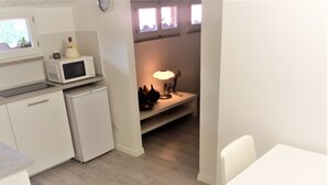 Eine kleine Küche mit einer Mikrowelle, einem kleinen Kühlschrank und einem Regal mit Schuhen und einer Lampe.