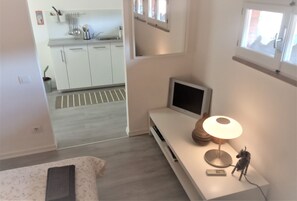 Una habitación de hotel moderna con una cama, una mesita de noche con lámpara, un televisor y vistas a la cocina.
