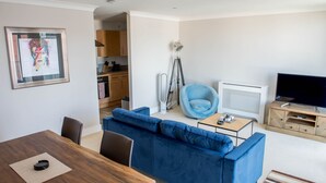 Un saló modern amb un sofà blau, una taula de dinar de fusta, un armari blau i un televisor sobre un suport de fusta.