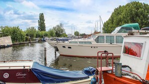 A marina with several boats docked, a covered area with a blue tarp, and a building with a sign reading "Doortje Amsterdam". - Beautiful (sta)caravan in Woubrugge (Woubrugge)