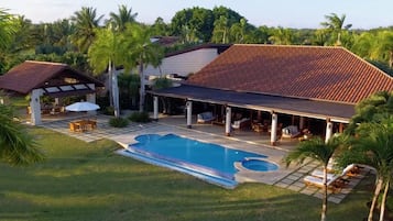 A resort with a swimming pool, covered patio, and lush greenery.