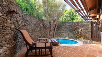 Un patio con pareti in pietra, una piscina, mobili in legno e un pergolato.