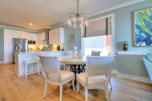 A modern kitchen with white cabinetry, a central island, and a dining area with four chairs. - 🌸Lilypad B: Oceanfront Duplex, 2 Decks w/ Beach Views🌸 (Kure Beach)
