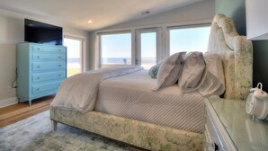 A bedroom with a bed, a dresser, a television, and a view of the beach. - 🌸Lilypad B: Oceanfront Duplex, 2 Decks w/ Beach Views🌸 (Kure Beach)
