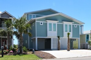 A two-story house with a flat roof, a garage, and a front yard with palm trees and a mailbox. - 🌸Lilypad B: Oceanfront Duplex, 2 Decks w/ Beach Views🌸 (Kure Beach)
