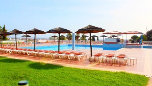 Un espace aménagé au bord de la piscine, avec des chaises longues et des parasols, une piscine, et un bâtiment en arrière-plan.