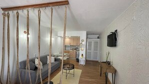 Une pièce avec un fauteuil suspendu, un canapé, une table à manger et, au fond, une cuisine.