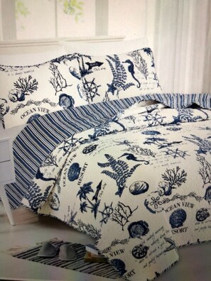 Una cama con cubrecama de tema náutico que presenta ilustraciones marinas, incluyendo un timón y criaturas marinas.