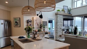 A modern kitchen with a central island, stainless steel appliances, wicker pendant lights, and a stone accent wall. - EXCLUSIVE LAKEFRONT PENTHOUSE *PRIVATE ROOFTOP DECK * POOL *HOTUB *SUNSET VIEWS  (Kelowna)