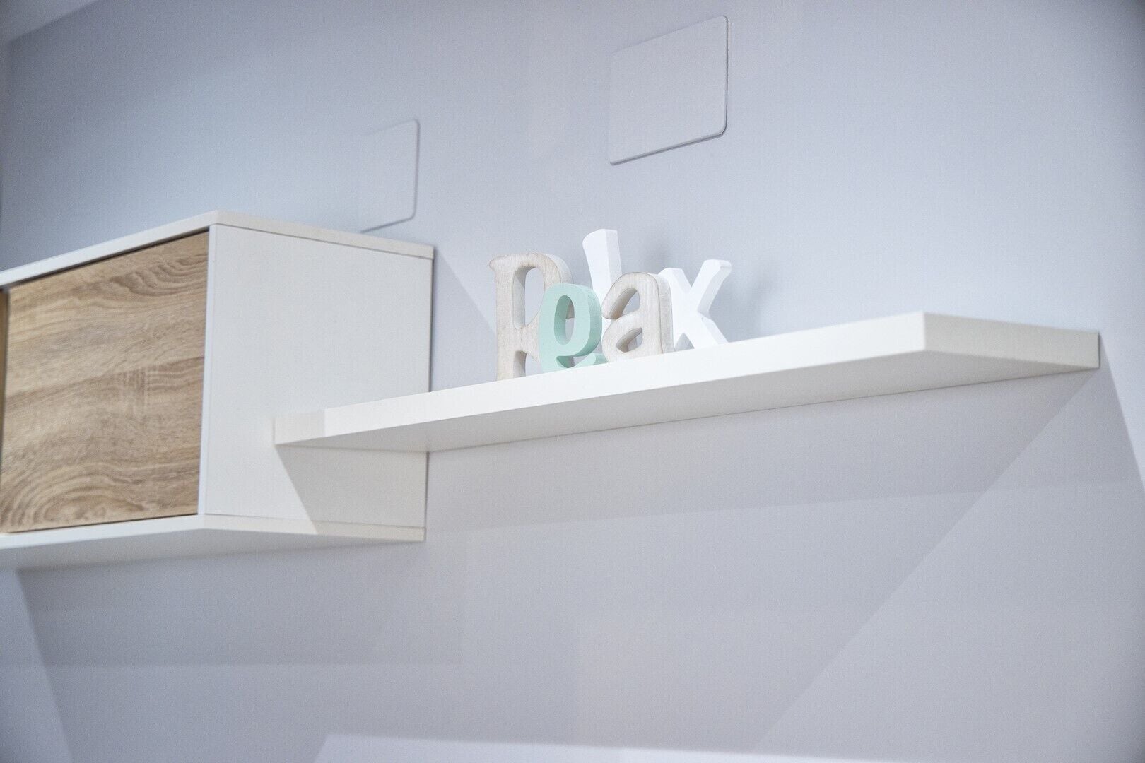 A white shelf with the word "Relax" in a playful font, mounted on a light gray wall.