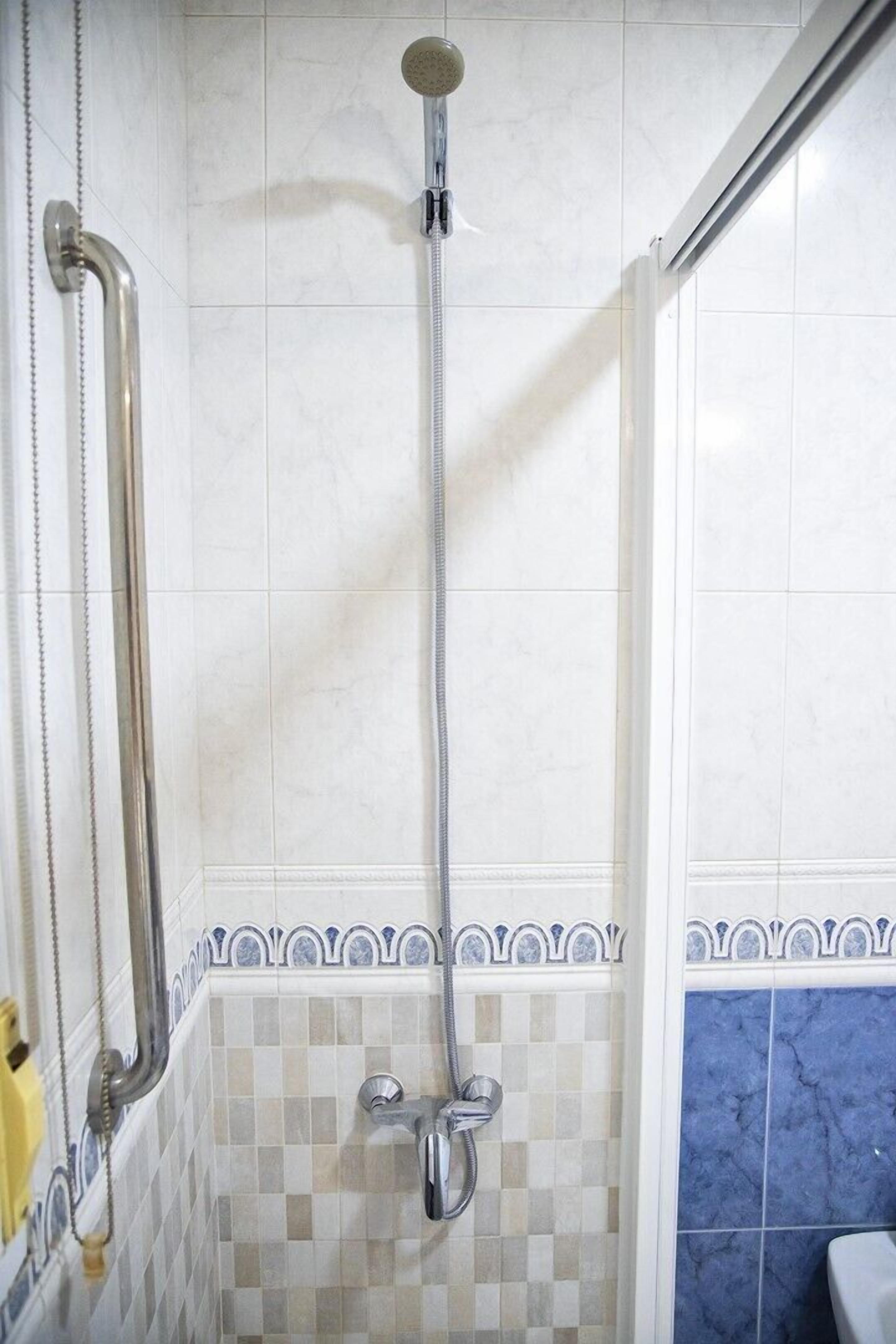 A shower with a handheld showerhead and a wall-mounted faucet.