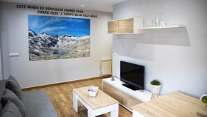 Un salon moderne avec une grande affiche représentant un paysage de montagne, un téléviseur à écran plat et des meubles au design minimaliste.