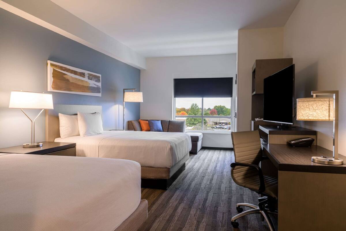 Une chambre d’hôtel avec deux lits, un bureau, une télévision et une fenêtre donnant sur des arbres.