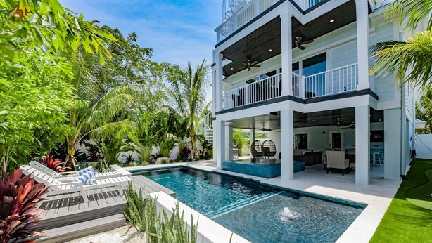 A two-story house with a swimming pool, outdoor seating, and lush greenery. - Putting green, Rooftop Deck AND Beach/Gulf Views with Private Heated Pool/Spa. (Lido Key)