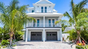 A two-story house with a balcony, two garages, and surrounded by palm trees. - Putting green, Rooftop Deck AND Beach/Gulf Views with Private Heated Pool/Spa. (Lido Key)