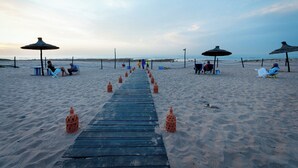 Een houten pad dat naar het strand leidt, met strandparasols en ligstoelen.