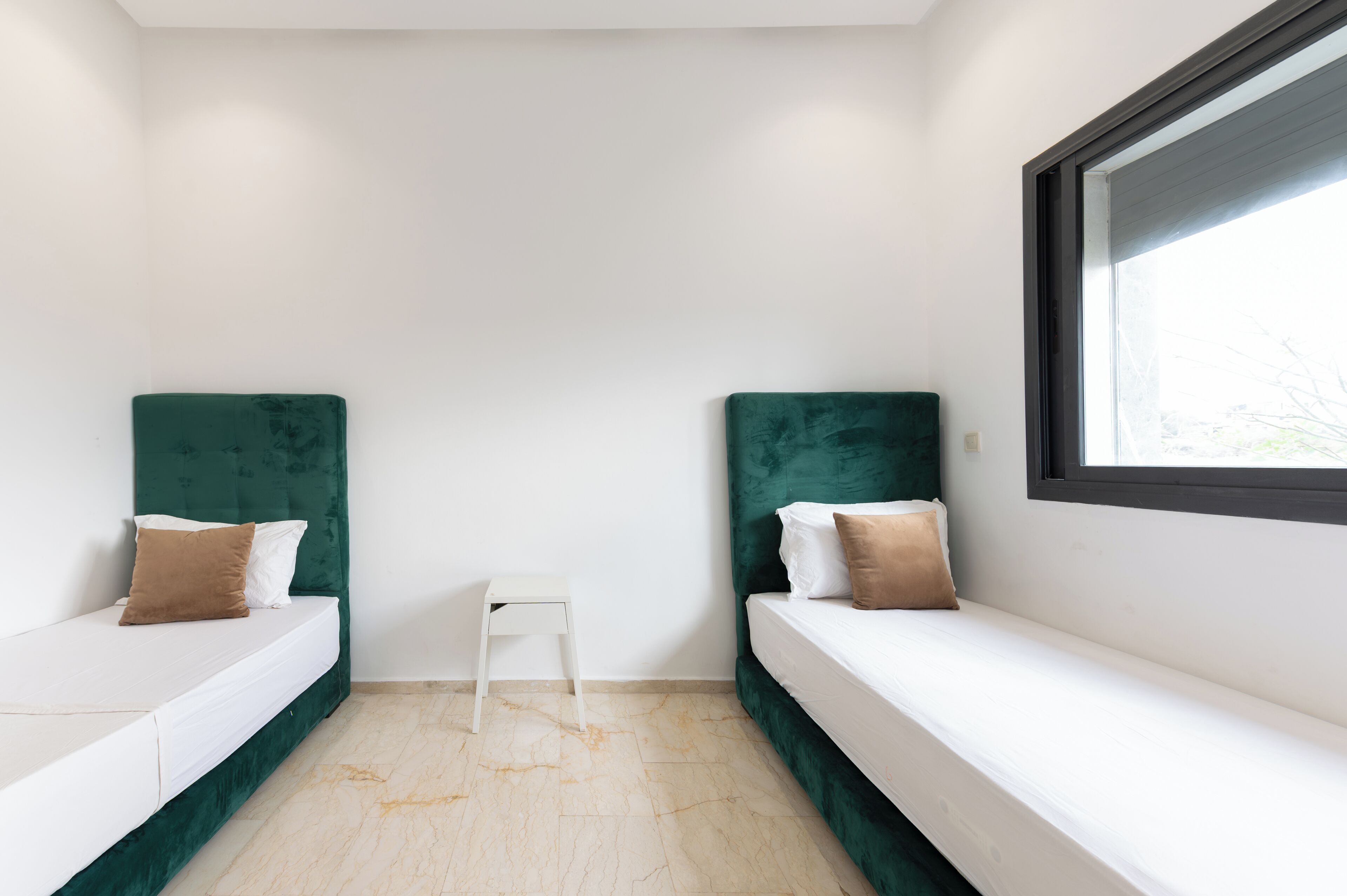A small, modern room with two beds, a small white table, and a window.