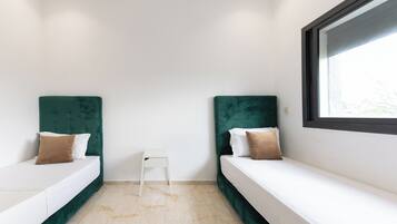 A small, modern room with two beds, a small white table, and a window.