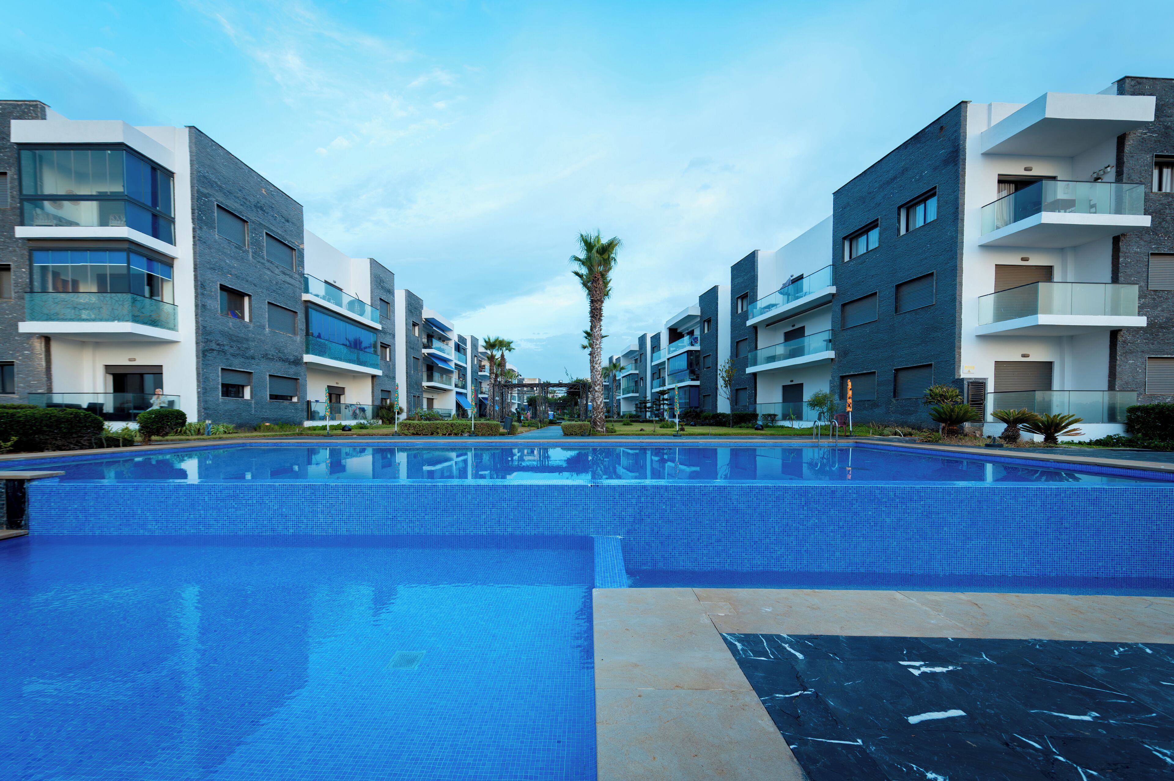 Ein modernes Hotel mit einem zentral gelegenen Schwimmbad, mehreren Balkonen und zeitgemäßer Architektur.