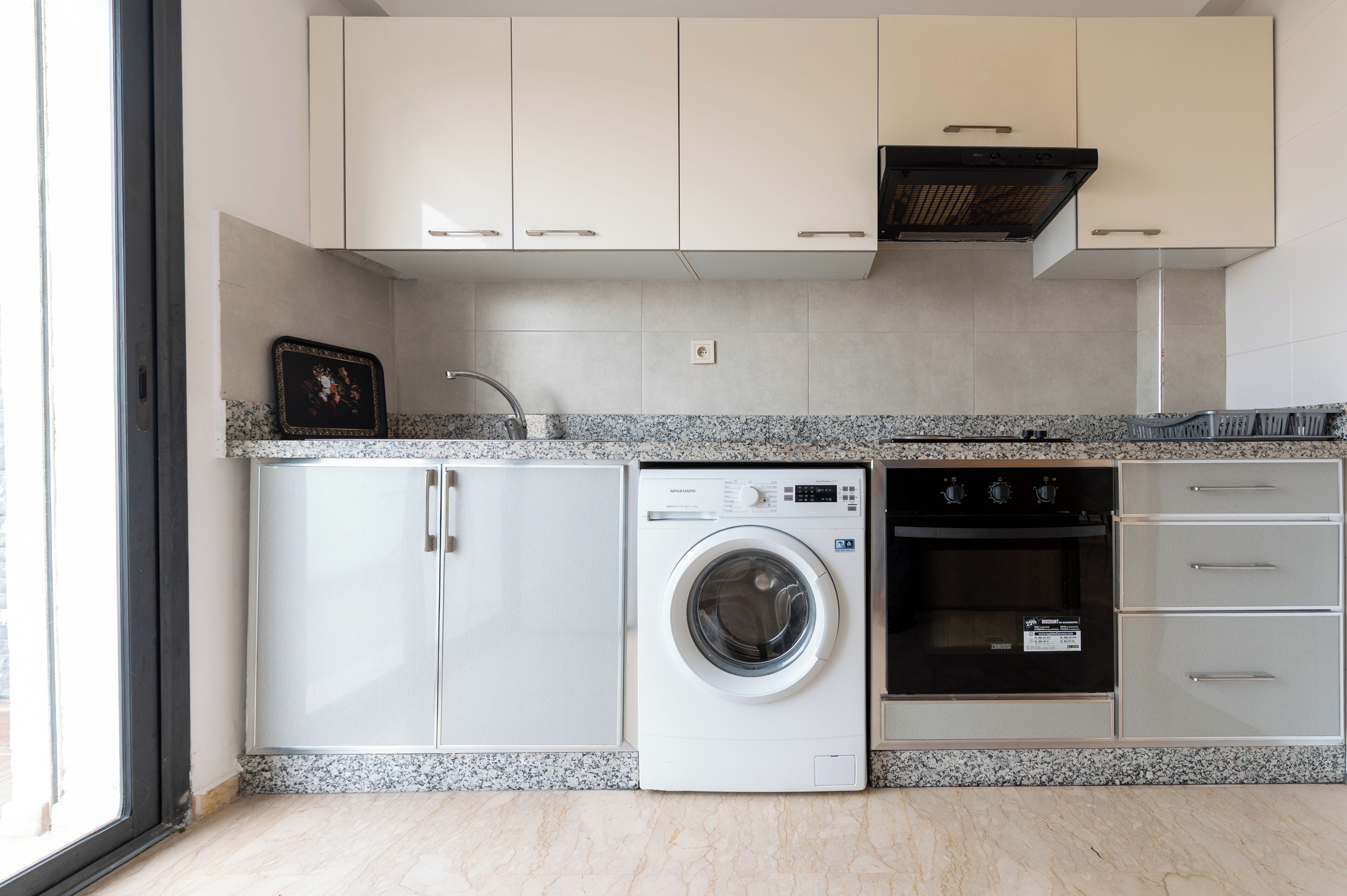 Una cocina moderna con armarios blancos, lavadora y secadora integradas, y un horno negro.