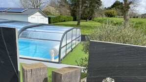 A swimming pool with a glass enclosure, surrounded by a wooden deck and a grassy lawn.