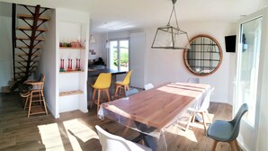 A dining area with a wooden table, yellow chairs, a white chair, a wooden ladder, and a hanging light fixture.