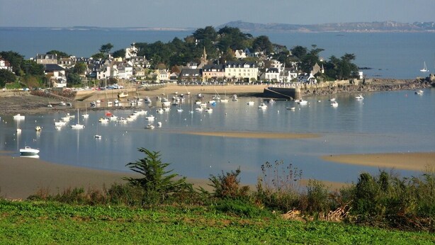 A coastal town with boats docked in the marina, buildings along the shore, and a sandy beach.