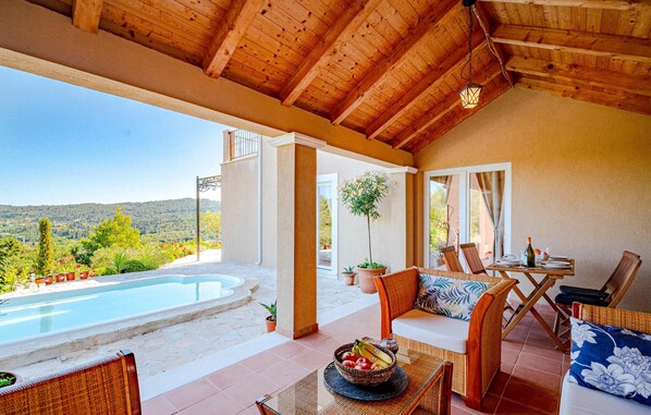 A covered outdoor seating area with a pool, wooden furniture, and a view of the landscape.