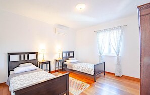 A bedroom with two beds, a window with floral curtains, a wooden floor, and a small bedside table with a lamp. - Beach front home in Zrnovo (Zrnovo)