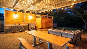 Eine Terrasse im Freien mit Holztisch und -bänken, einem Grill und einem Holzzaun.