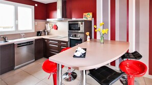A modern kitchen with a dining area, red and white striped walls, stainless steel appliances, and red bar stools. - Stunning home in Lussas (Lussas)
