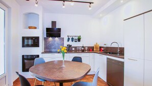 A modern kitchen with white cabinets, a built-in oven, a microwave, and a stove. There is a dining table with chairs, a vase with flowers, and a sink with a faucet. - Stunning home in Lussas (Lussas)