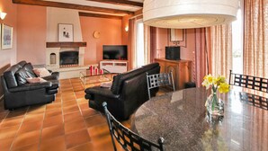 A living room with a fireplace, a TV, a dining table with chairs, and a large window with curtains. - Stunning home in Lussas (Lussas)