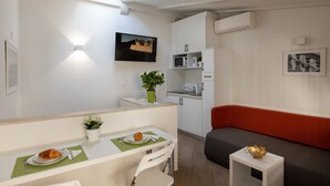 Et moderne køkken med hvide skabe, en mikrobølgeovn og en vask. Der er et spiseområde med et bord, stole og en plante. En rød sofa og et lille, hvidt sofabord er også synlige.